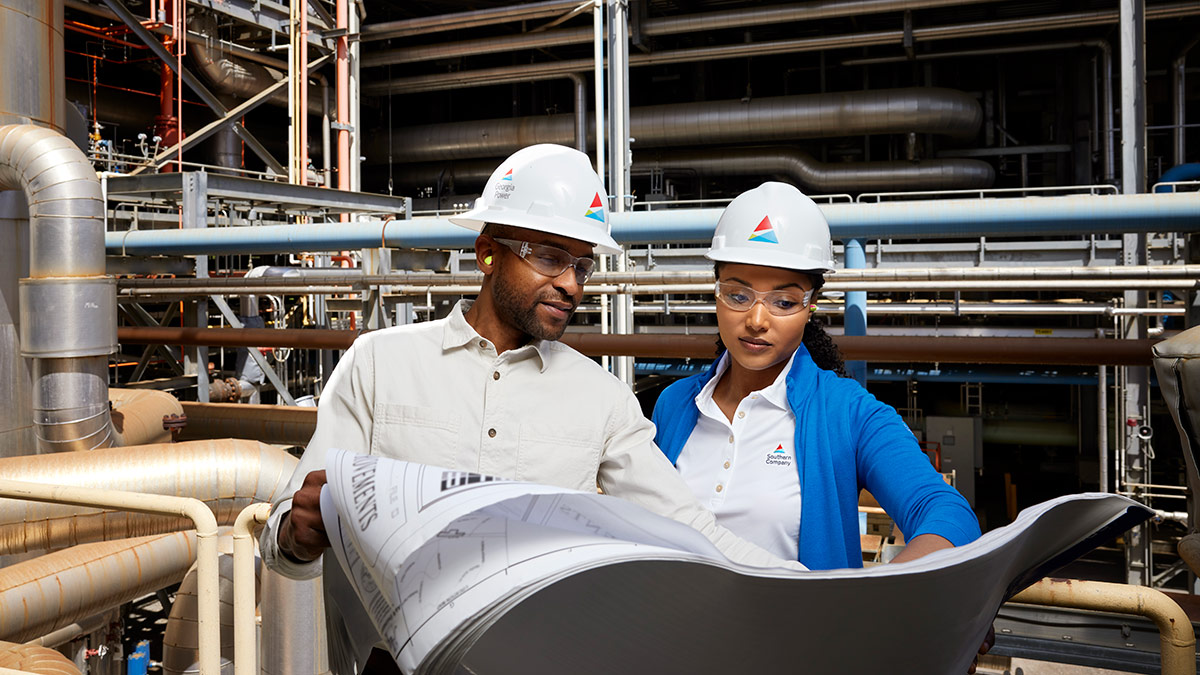 Man and a woman reviewing blueprints wearing hardhats at a power plant